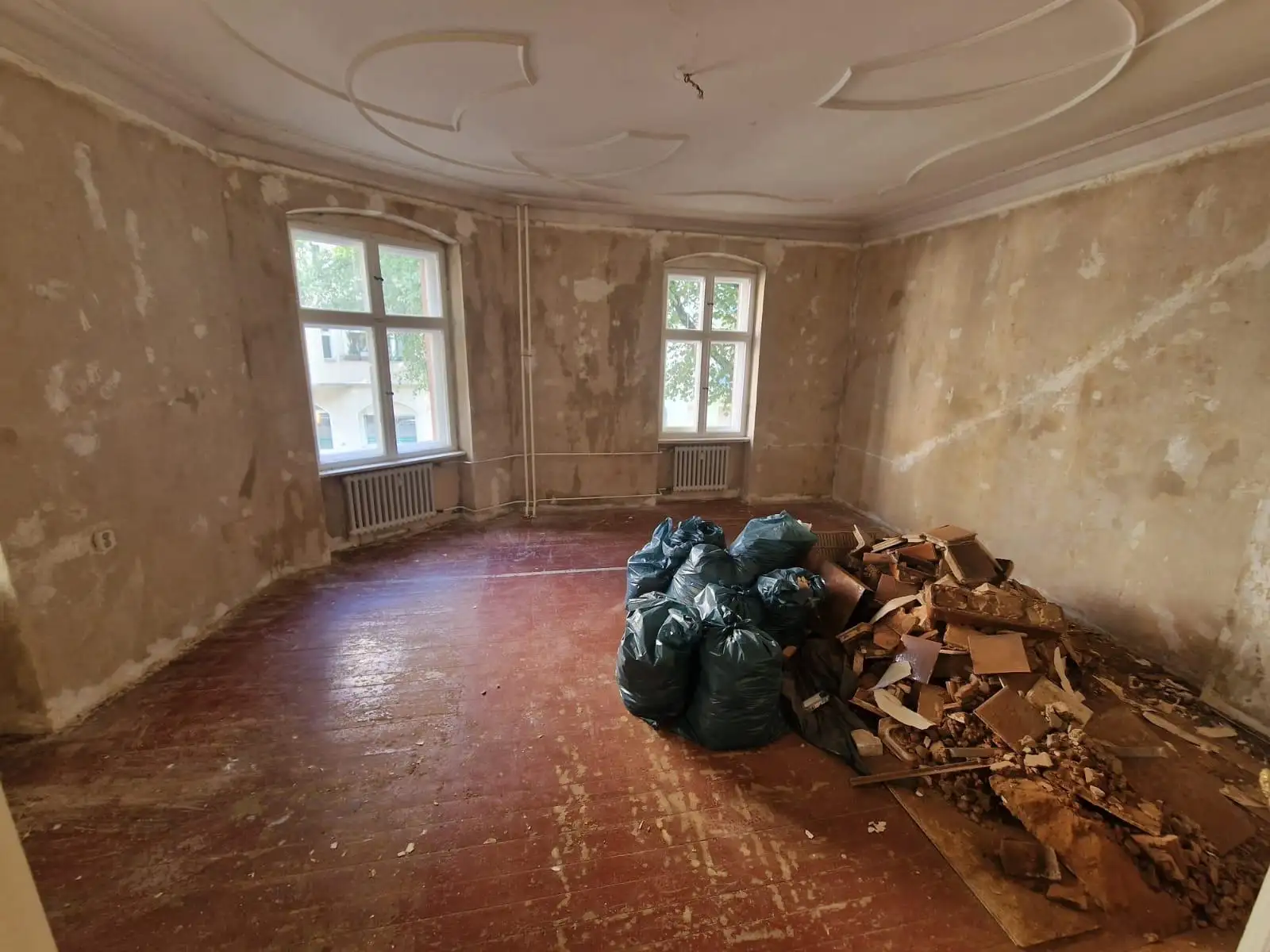 Wohnzimmer vor der Sanierung – beschädigte Wände, alter Boden, Bauschutt